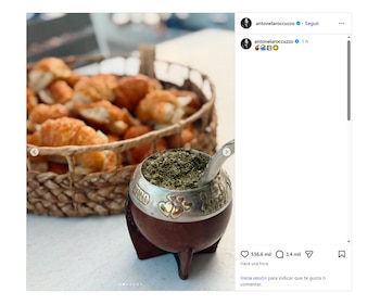 Un mate de calabaza con yerba y bombilla en primer plano, con una canasta tejida llena de medialunas de fondo en una mesa