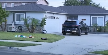Una casa residencial de un piso con techo oscuro y paredes claras. Un SUV negro estacionado en la entrada y algunos objetos esparcidos en el césped delantero