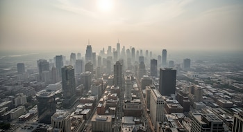 Vista aérea de una ciudad estadounidense con numerosos rascacielos bajo una densa neblina gris y el sol brillando débilmente a través de la calima.