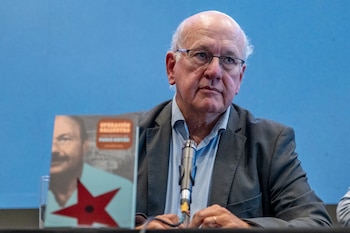 Primer plano de Pablo Sirvén, un hombre calvo de tez clara y gafas, sentado frente a un micrófono, con su libro "Operación Grial" visible a su izquierda, sobre un fondo azul