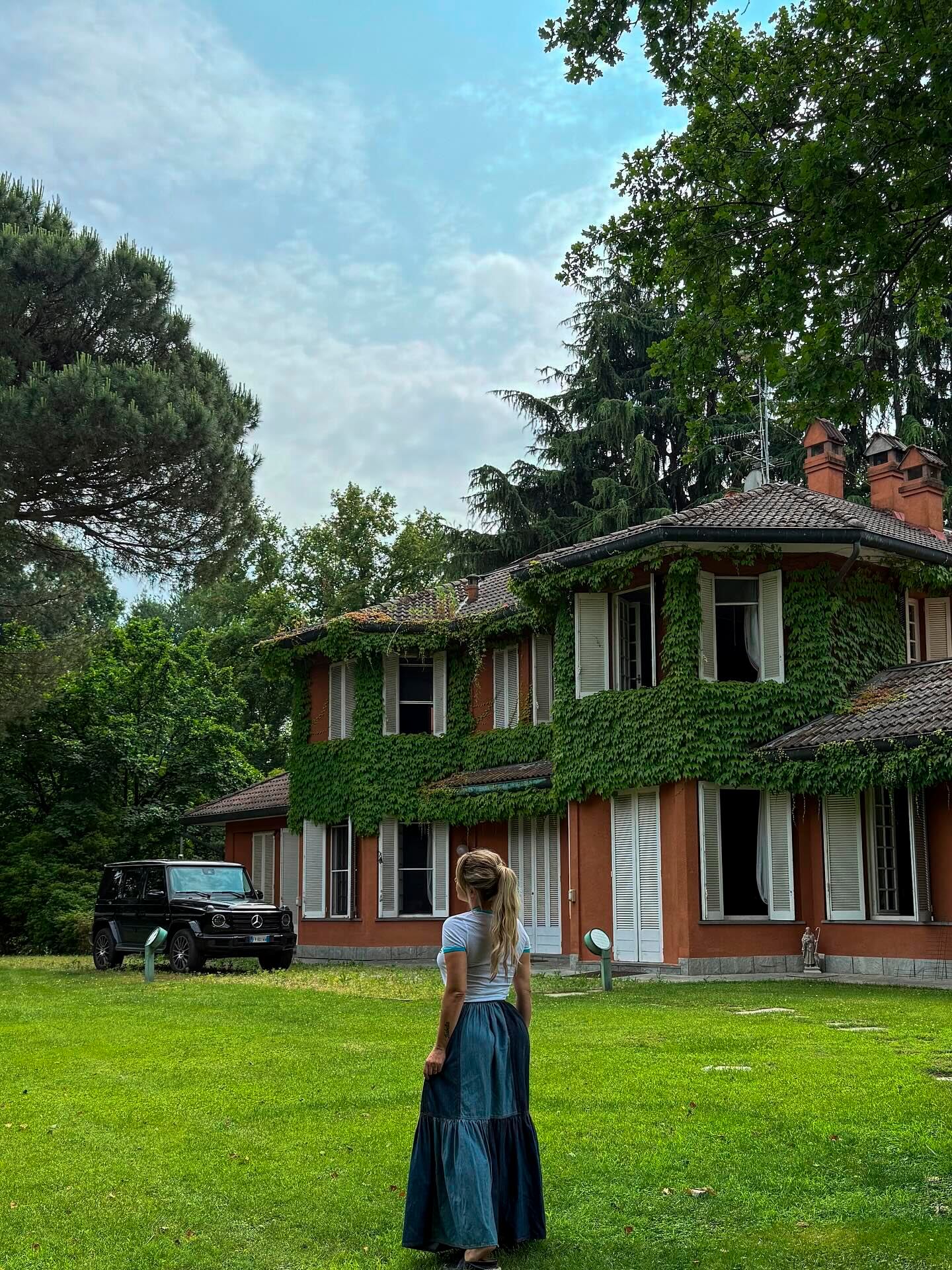 De espaldas, la empresaria posa en la entrada de su casa en Galliate, con la fachada cubierta de enredaderas y su Mercedes Benz (Instagram)