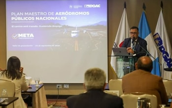 Un hombre habla en un atril junto a una pantalla de proyección que muestra un texto sobre aeródromos ante varias personas