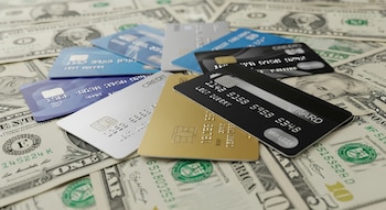 Varias tarjetas de crédito de diferentes colores (azules, plateada, negra y dorada) están dispuestas sobre billetes de un dólar estadounidense.