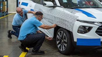 Dos hombres con camisetas azules y jeans agachados, aplicando un vinilo de camuflaje en blanco y negro a la parte delantera de un automóvil blanco