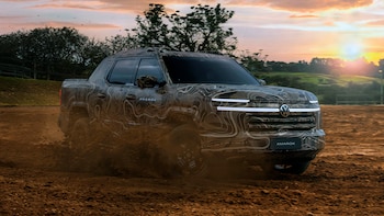 Camioneta todoterreno camuflada con el logotipo de Volkswagen avanza levantando tierra en un terreno rural al atardecer