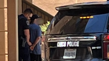 Un oficial de policía esposando a una persona vestida de azul y con gorra, frente a un SUV negro de la policía de Chico, visto desde atrás