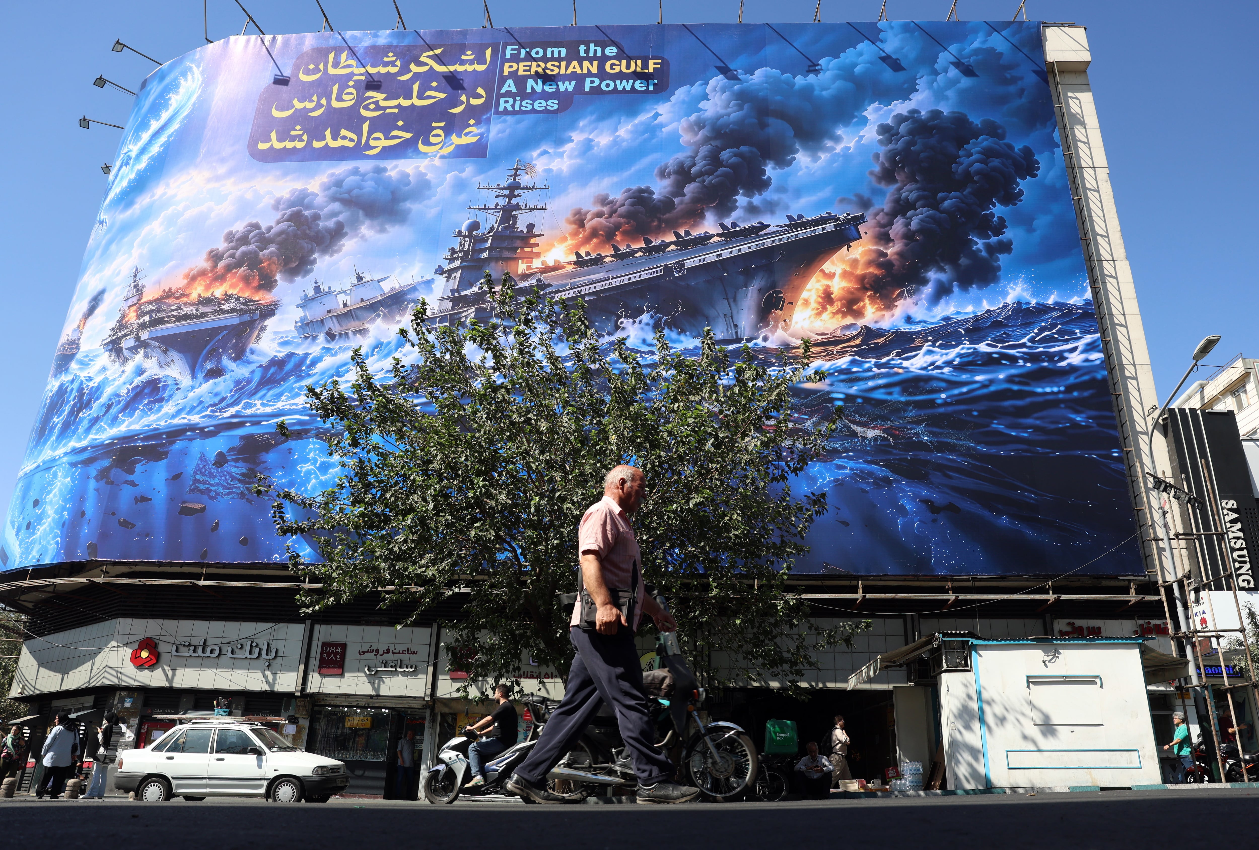 Iraníes caminan junto a una valla publicitaria antiamericana que muestra una frase en persa que dice: