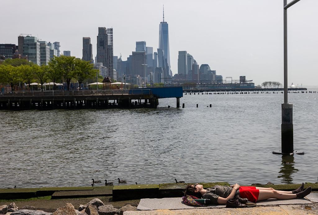 Una mujer toma sol junto al río Hudson mientras la ciudad atraviesa una primavera marcada por temperaturas récord y hábitos típicos del verano adelantados varias semanas.