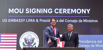 Dos hombres de traje se dan la mano frente a una pantalla con el texto en inglés MOU SIGNING CEREMONY y las banderas de Estados Unidos y Perú