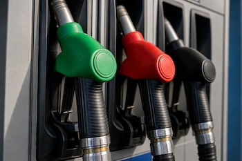 Tres pistolas de surtidor de combustible con cubiertas de color verde, rojo y negro alineadas en sus soportes metálicos.