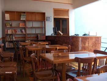 Interior de una biblioteca con varias mesas y sillas de madera. A la izquierda, estanterías con libros. A la derecha, un mostrador con una computadora