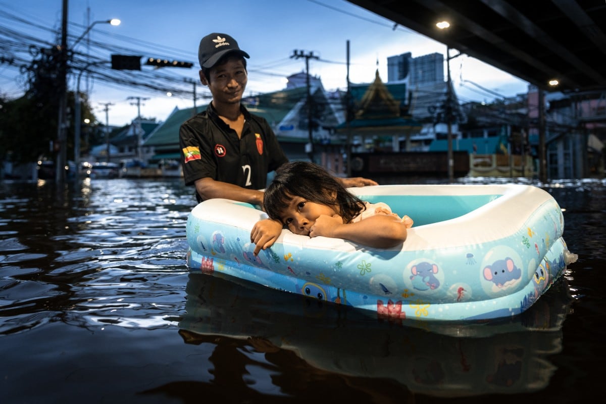 Un hombre arrastra a una niña en un bote inflable por las aguas de la inundación en Bang Kapi, Bangkok. En una calle del este de la ciudad el agua llegó a la cintura (Chanakarn Laosarakham/AFP)