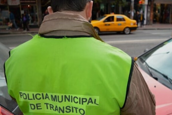 Vista posterior de una persona con un chaleco reflectante amarillo con la leyenda Policía Municipal de Tránsito y un taxi amarillo al fondo