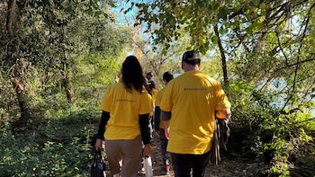 Personas de espaldas con camisetas amarillas con la inscripción VoluntariosEY caminan por un sendero entre árboles