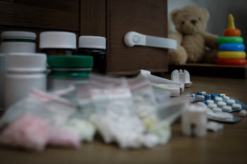 Frascos de medicinas, bolsas con comprimidos, dispositivos de seguridad para cajones y juguetes sobre una mesa de madera.