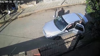 Vista desde arriba de un automóvil plateado con las puertas abiertas y dos personas con ropa oscura en una calle