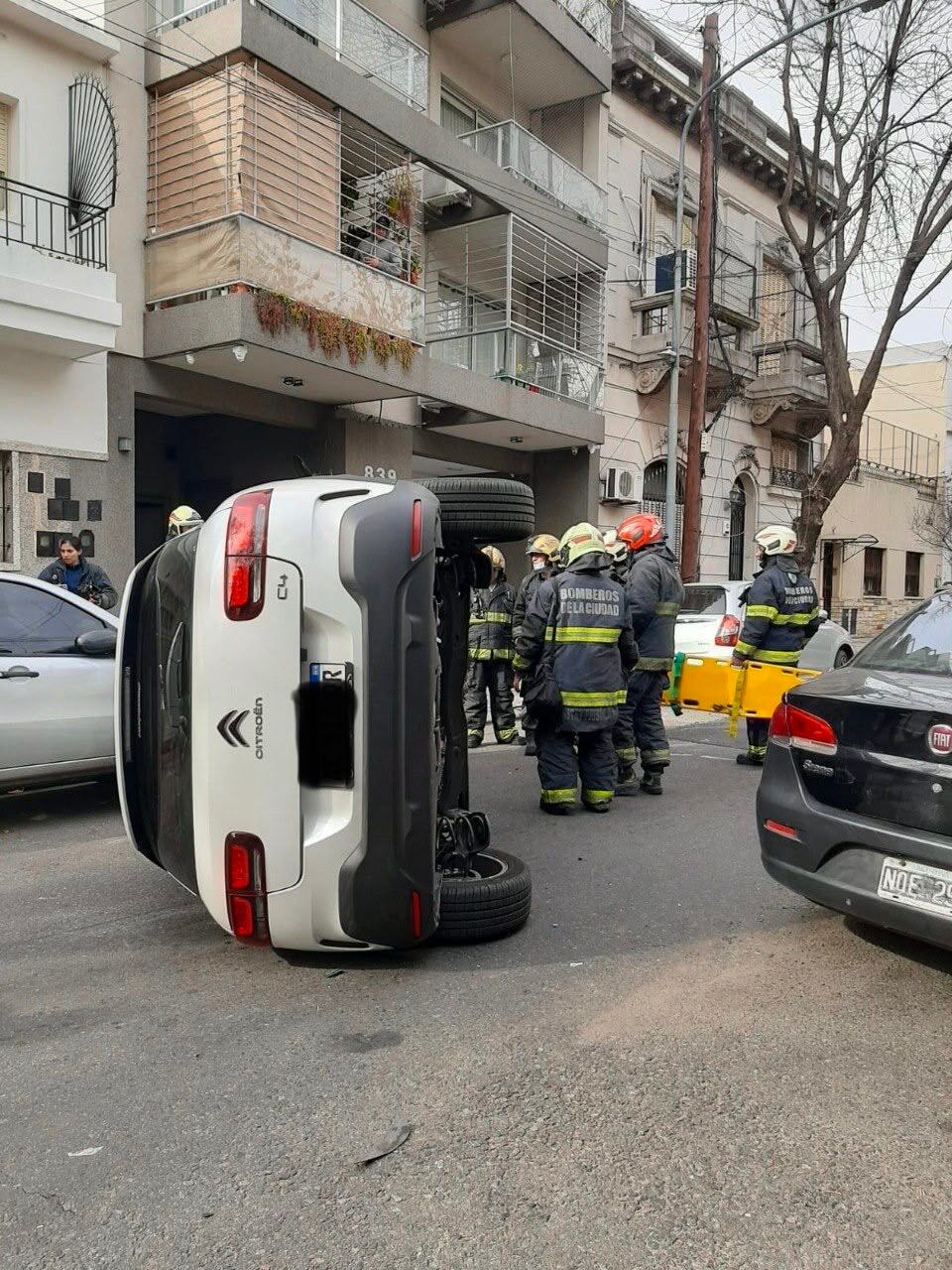 Bomberos de la Ciudad asisten en la escena de un vehículo Citroën C4 volcado lateralmente sobre el asfalto en una calle de Flores
