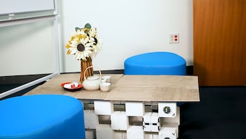 Mesa baja de base modular blanca y tablero de madera con un florero y un juego de té, flanqueada por dos taburetes azules