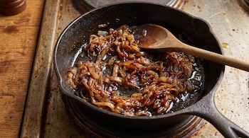 Sartén de hierro con cebolla dorada y caramelizada junto a una cuchara de madera.