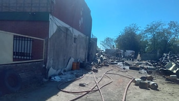 Edificios parcialmente destruidos, montones de escombros, mangueras de bomberos y cilindros de gas en el suelo bajo un cielo azul brillante