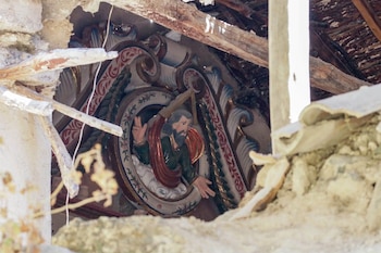 Techo y muro destruidos de una iglesia, con escombros y vigas de madera rotas; se ve un detalle artístico con la figura de un hombre barbudo