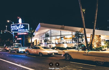 Automóviles clásicos de época en una calle nocturna frente a un restaurante iluminado con un cartel de neón de Mel's Drive-In