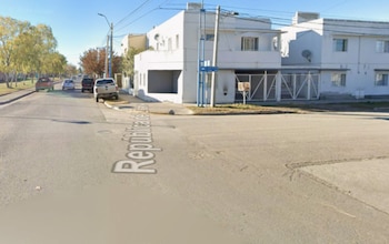 Una esquina urbana con casas blancas, autos estacionados, árboles y la frase República del Líbano sobre el asfalto