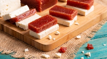 Close-up de sanduíche de goiaba vermelha com queijo branco na tábua de madeira. O fundo consiste em estopa e um padrão azul.