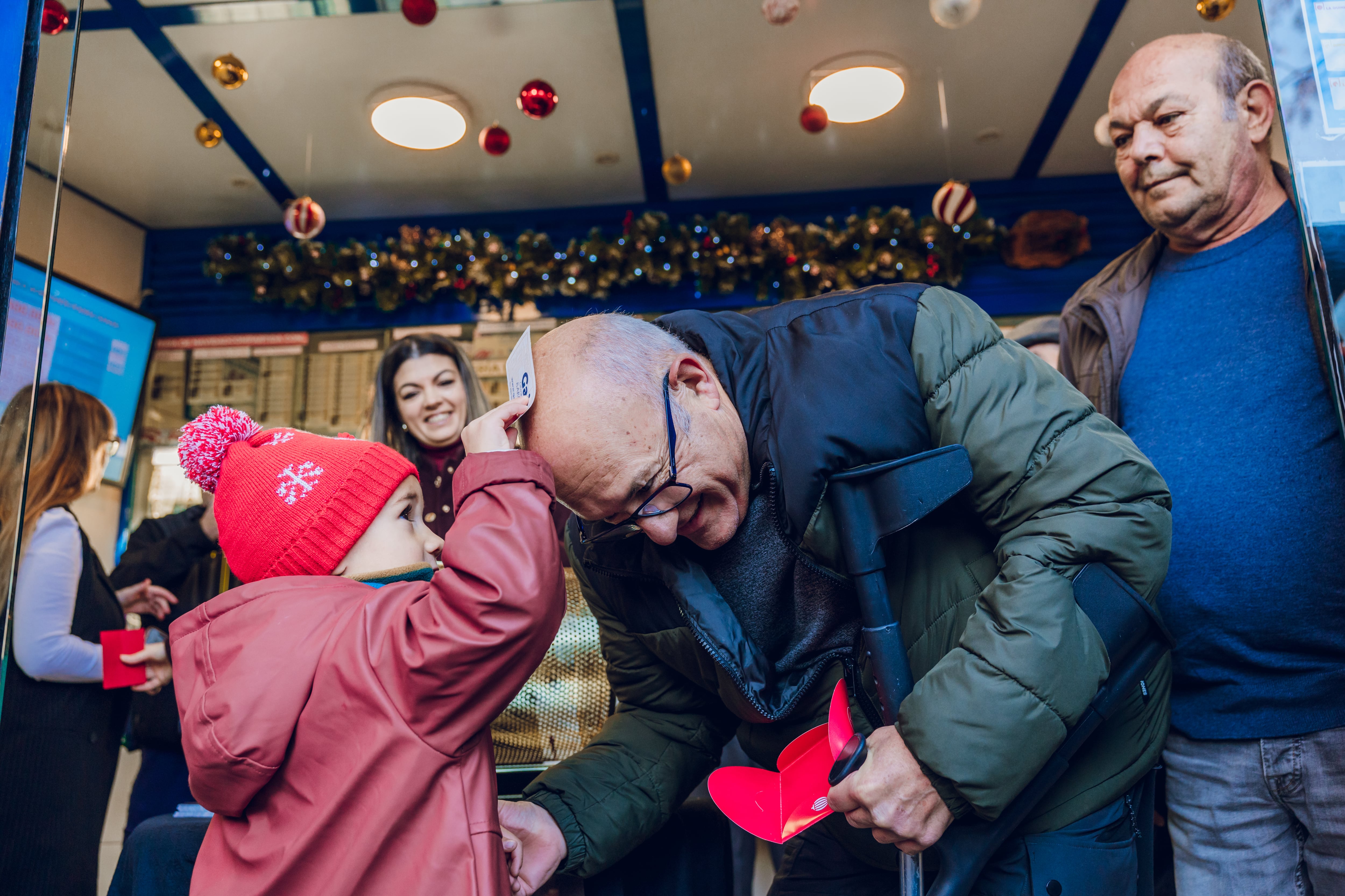 Un niño frota un décimo de Lotería de Navidad en la cabeza de un señor calvo. (Míriam Vázquez)