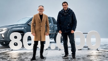 Dos hombres sonríen junto a una camioneta pickup gris y números blancos gigantes que forman 800.000 sobre un suelo cubierto de nieve