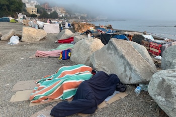 Varias personas migrantes duermen en la playa del Trampolín en Ceuta. (EFE/Reduan)