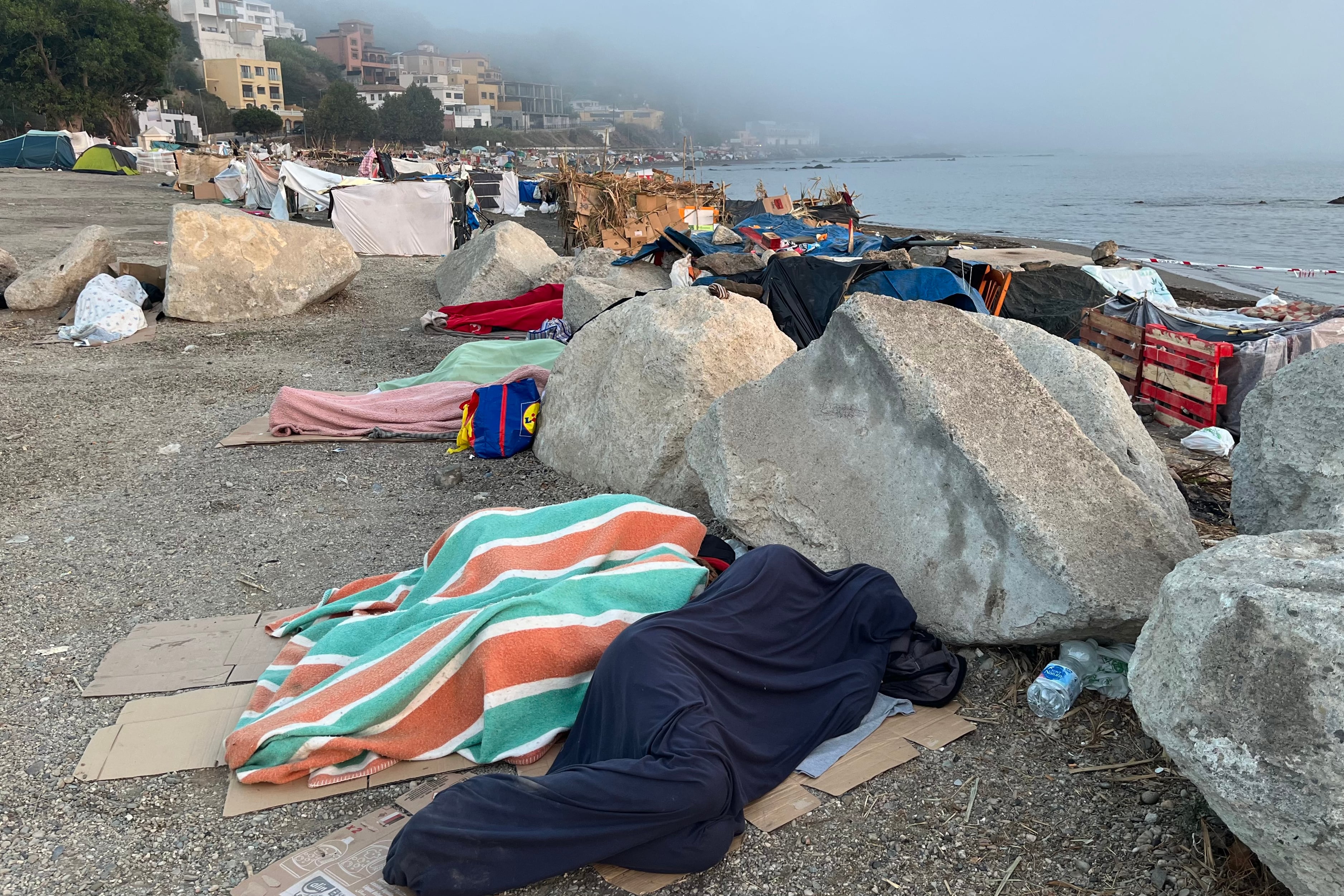 Varias personas migrantes duermen al raso en la playa del Trampolín en Ceuta. (EFE/Reduan)