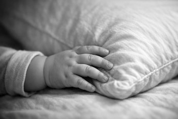 Primer plano en blanco y negro de la mano de un bebé de 14 meses reposando sobre una almohada. Se aprecia la textura suave de la tela.