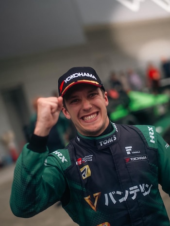 Sacha Fenetraz, con gorra "Yokohama" y traje de piloto de carreras verde oscuro y negro, sonríe ampliamente y levanta el puño derecho