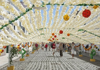 Personas caminan por una calle empedrada bajo un techo de flores de papel blanco y adornos colgados