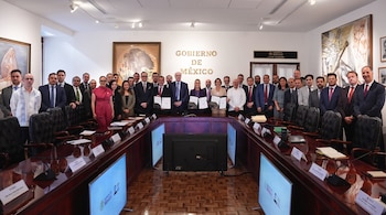 Un grupo de hombres y mujeres en ropa formal posa tras una mesa de conferencias frente a una pared con la inscripción Gobierno de México.