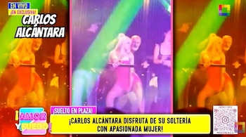 Carlos Alcántara, hombre calvo con barba, observa a una mujer rubia con traje rosado-rojo en un escenario iluminado con luces verdes y rojas