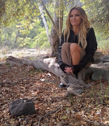 Sofía Zámolo sentada en un bosque, rodeada de hojas secas y árboles, viste chaqueta negra y falda beige, con una sonrisa leve