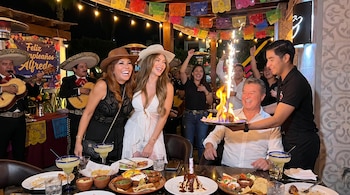 Magaly Medina y Sheyla Rojas sonriendo con sombreros. Alfredo Zambrano con postre flamígero, mariachis tocando, y comida mexicana en un restaurante.