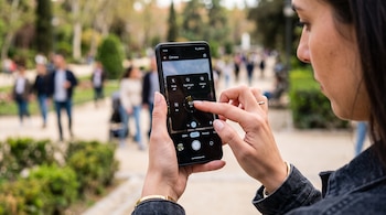 Manos de una persona que sostienen un teléfono móvil y ajustan los controles de la cámara en la pantalla.
