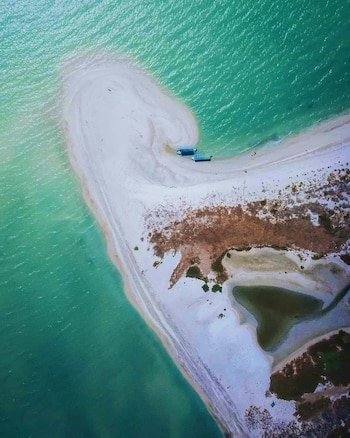 Vista aérea de una lengua de arena blanca rodeada por agua turquesa con dos embarcaciones azules cerca de la orilla