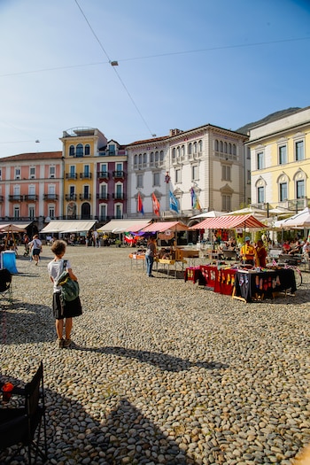 Una parte de la plaza con adoquines de piedra de río, como cantos rodados, y una chica mirando los puestos de un mercado que hay