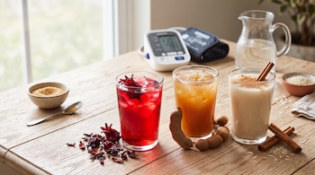 Tres vasos con agua de jamaica, tamarindo y horchata sobre una mesa de madera junto a un tensiómetro digital y una jarra de agua.