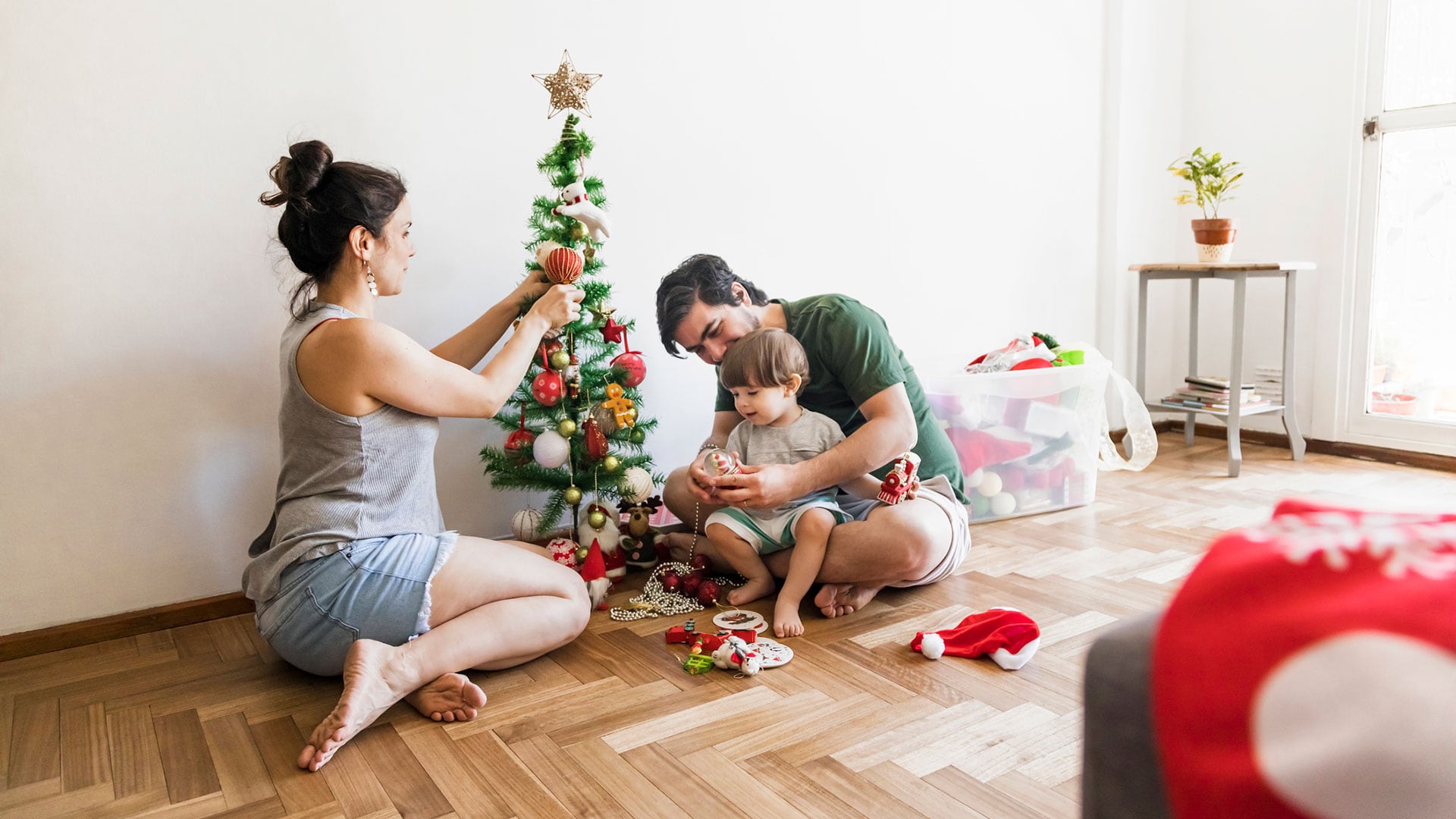 Latin American family of 3 (mother, father and 1 year-old son) decorating Christmas tree during Summer season in Argentina. Copy space. (Getty)