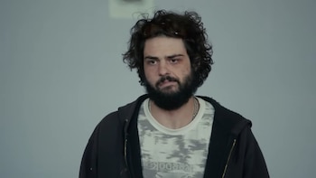 El actor Noah Centineo tiene cabello rizado oscuro, barba y bigote. Viste sudadera con capucha negra, camiseta blanca con estampado y cadena plateada