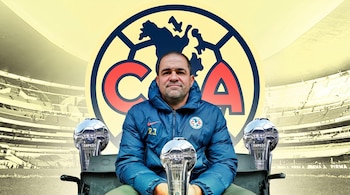 Hombre sentado con chaqueta azul sostiene un trofeo "CAMPEÓN CLAUSURA 2024", con otros dos trofeos similares, sobre fondo del escudo del Club América y un estadio.