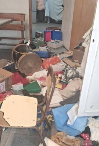 Piso cubierto de objetos esparcidos, incluyendo ropa, cajas, una silla rota, un bombo y bolsas en un interior