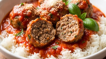 Albóndigas en salsa de tomate con queso y albahaca, servidas sobre arroz blanco en un tazón. Una albóndiga está cortada mostrando su interior de carne.