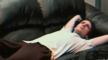 Jeff Buckley tumbado en un sofá oscuro, con una camiseta clara y pantalones oscuros, mirando hacia arriba con su brazo derecho detrás de la cabeza
