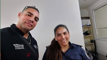 Un hombre con camiseta negra que dice "Secretaría de Protección Ciudadana" y una mujer con camisa azul sonríen. Fondo blanco con estante y archivos
